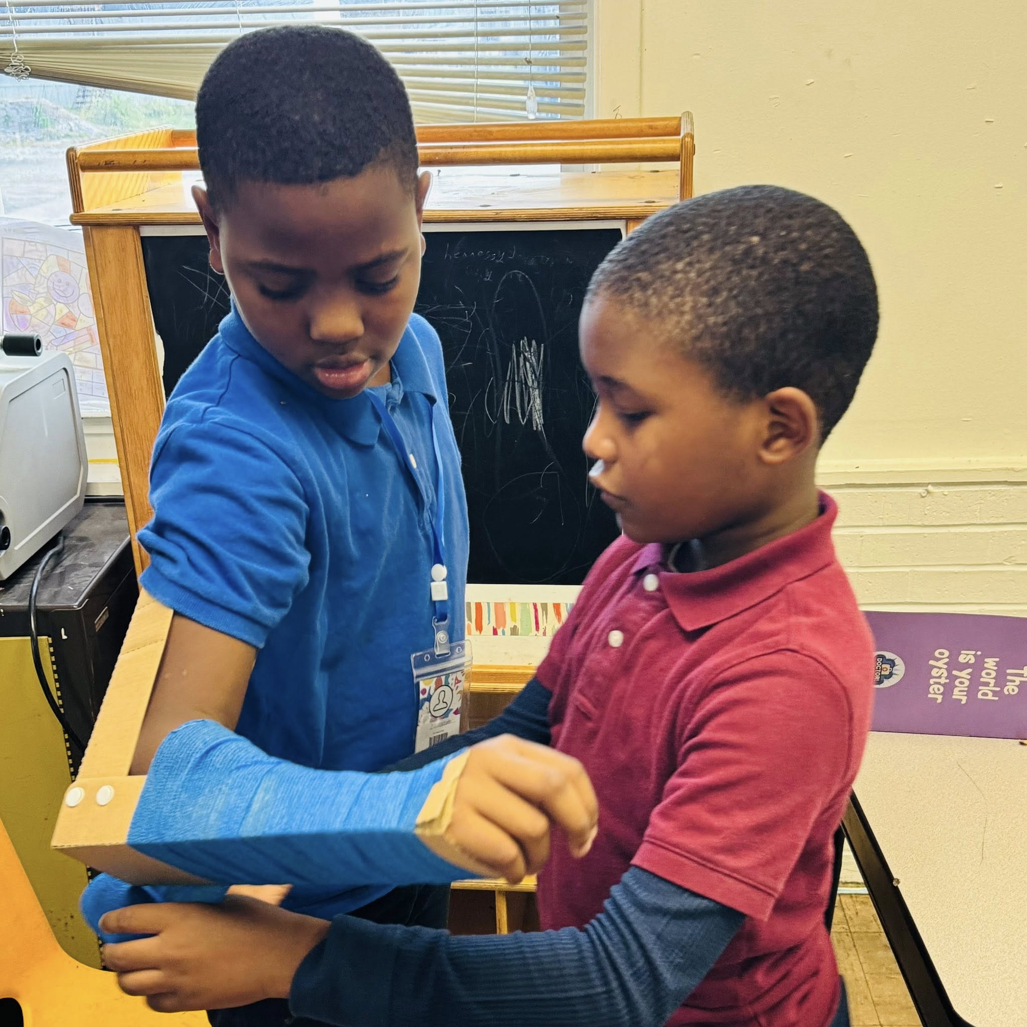 A little boy putting a splint on another boy's arm.
